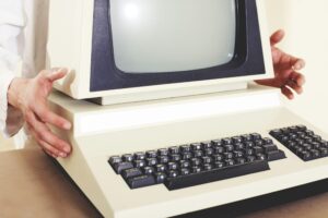 A vintage computer with a classic CRT monitor and keyboard, being held by hands.