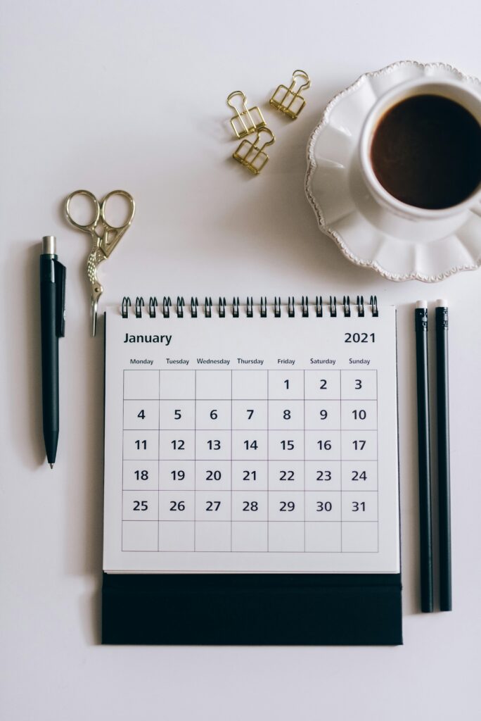 pexels-photo-5408818-5408818 Flat lay of a 2021 desk calendar, coffee cup, and black stationery items on a white surface.
